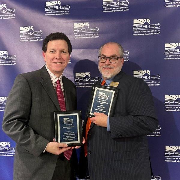 Mark Kovacs and Gary Leising hold up plaques at the Genesis Group's Celebration of Education event in November 2023.